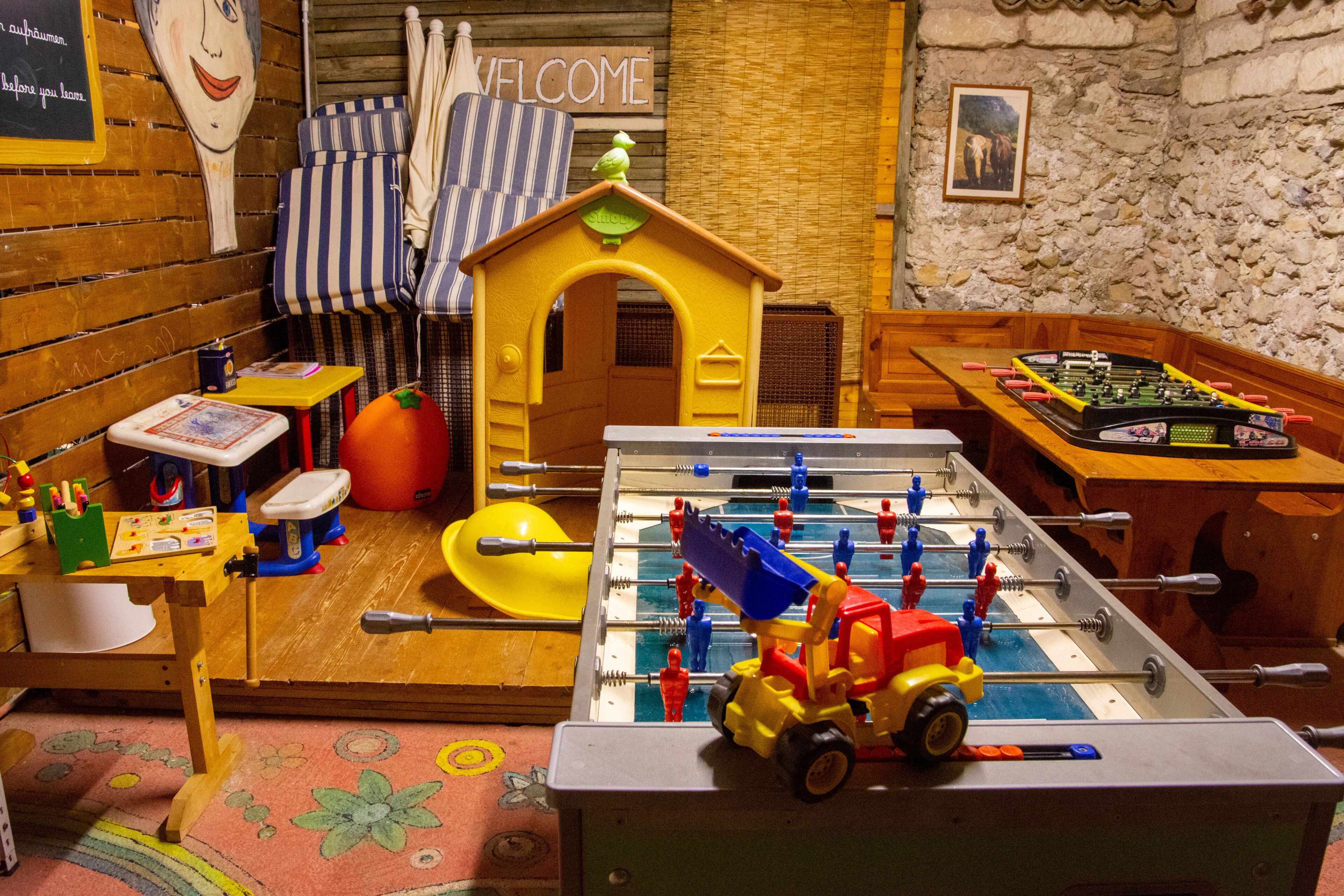 Ein Kinderspielbereich mit einem Tischfußballtisch, einem kleinen Haus und einem Willkommensschild.