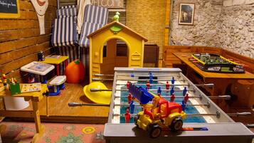 Ein Kinderspielbereich mit einem Tischfußballtisch, einem kleinen Haus und einem Willkommensschild.