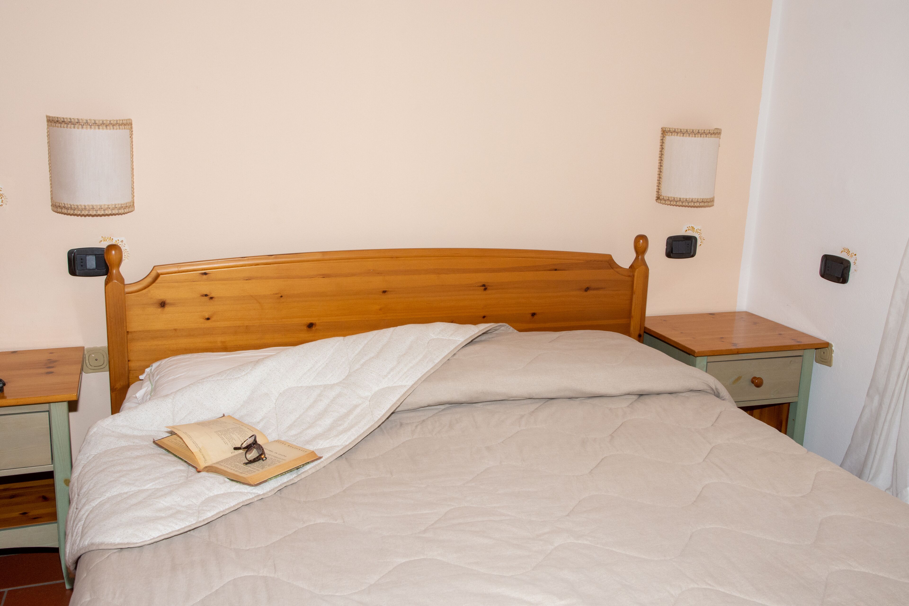 A neatly made bed with a wooden headboard, two bedside tables with lamps, and a small bedside drawer.
