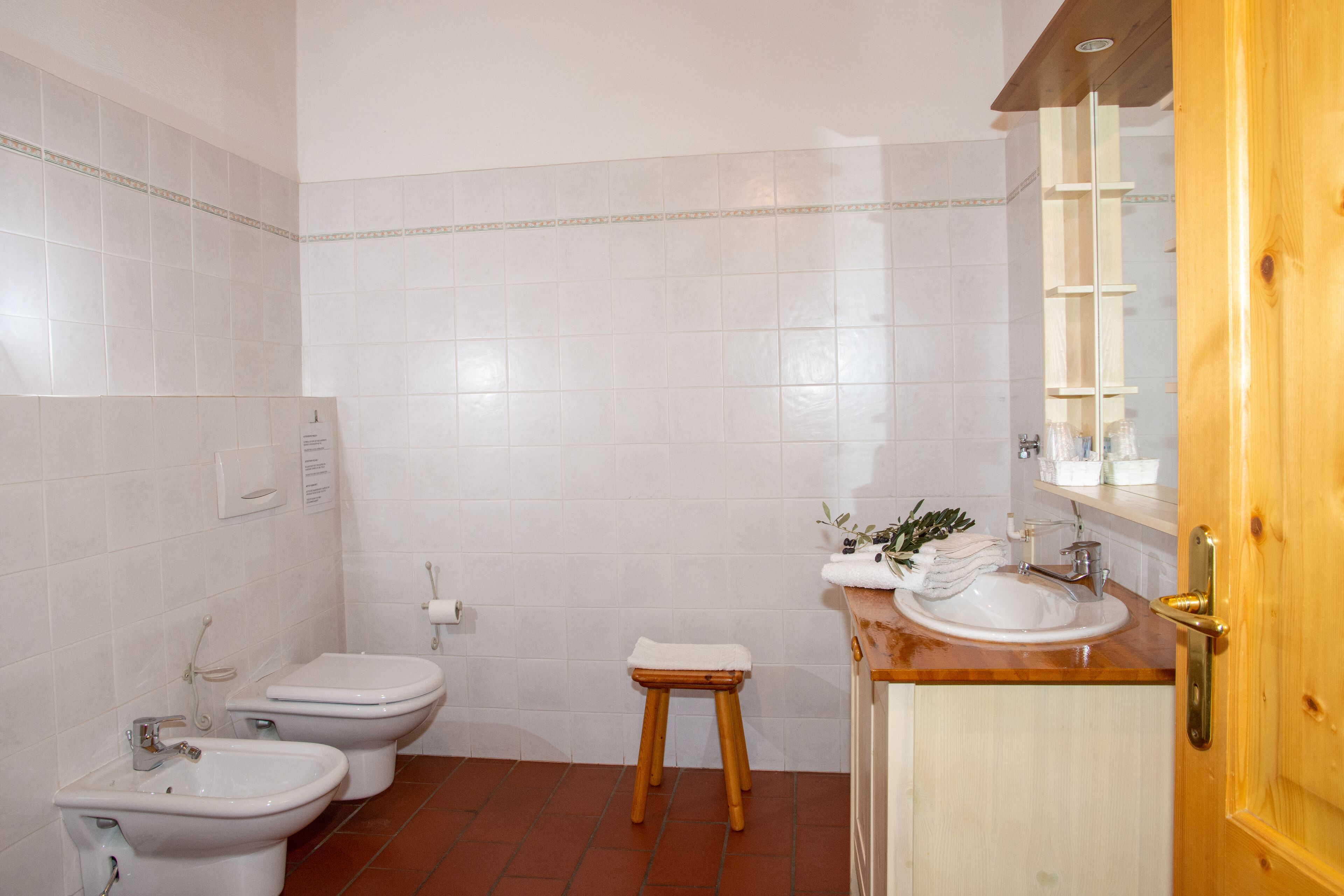 Ein Badezimmer mit weißen Fliesen, einem Holzschemel, einem Waschbecken und einer Toilette.