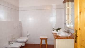 A bathroom with white tiles, a wooden stool, a sink, and a toilet.