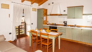 Une cuisine chaleureuse avec des meubles de rangement en bois, une table à manger avec des chaises et une fenêtre agrémentée de rideaux.