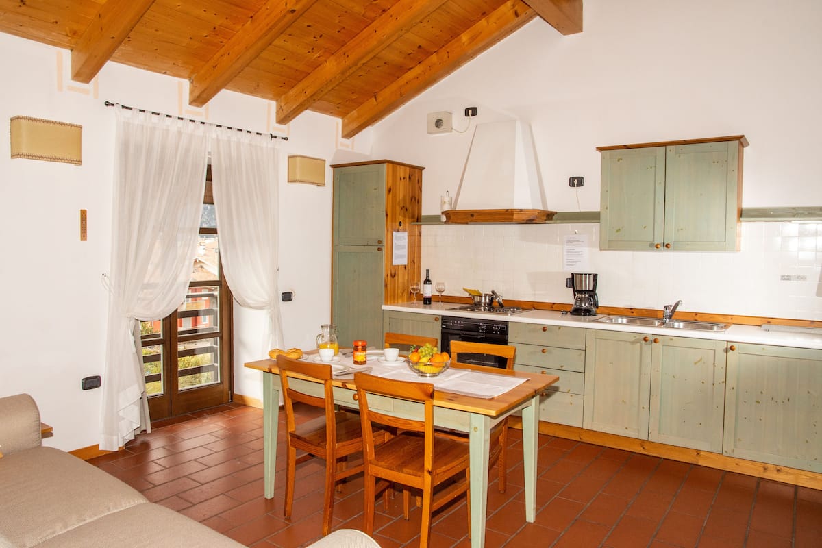 Une cuisine chaleureuse avec des meubles de rangement en bois, une table à manger avec des chaises et une fenêtre agrémentée de rideaux.