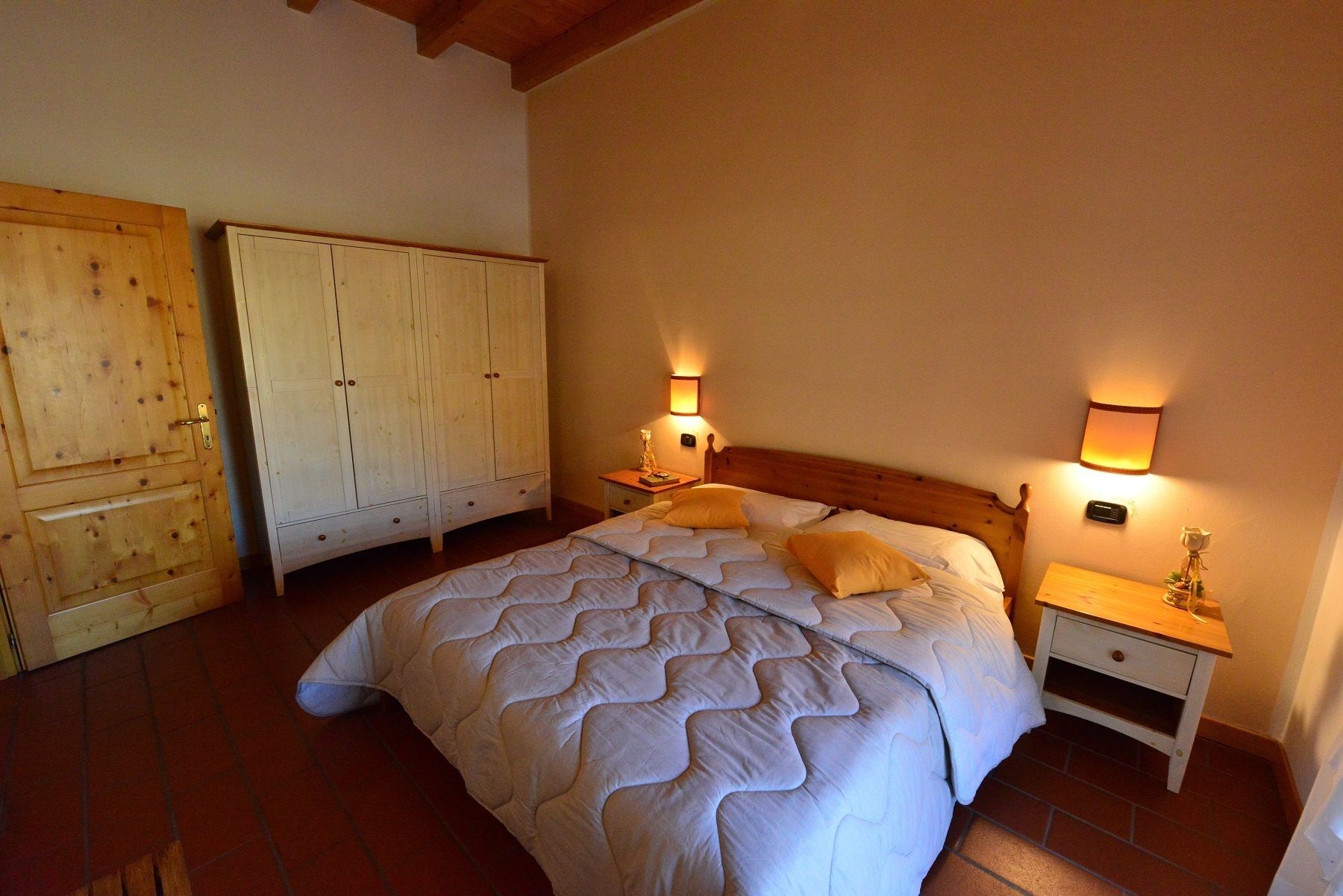 A bedroom with a large bed, two nightstands, wooden wardrobes, and wall-mounted lamps.