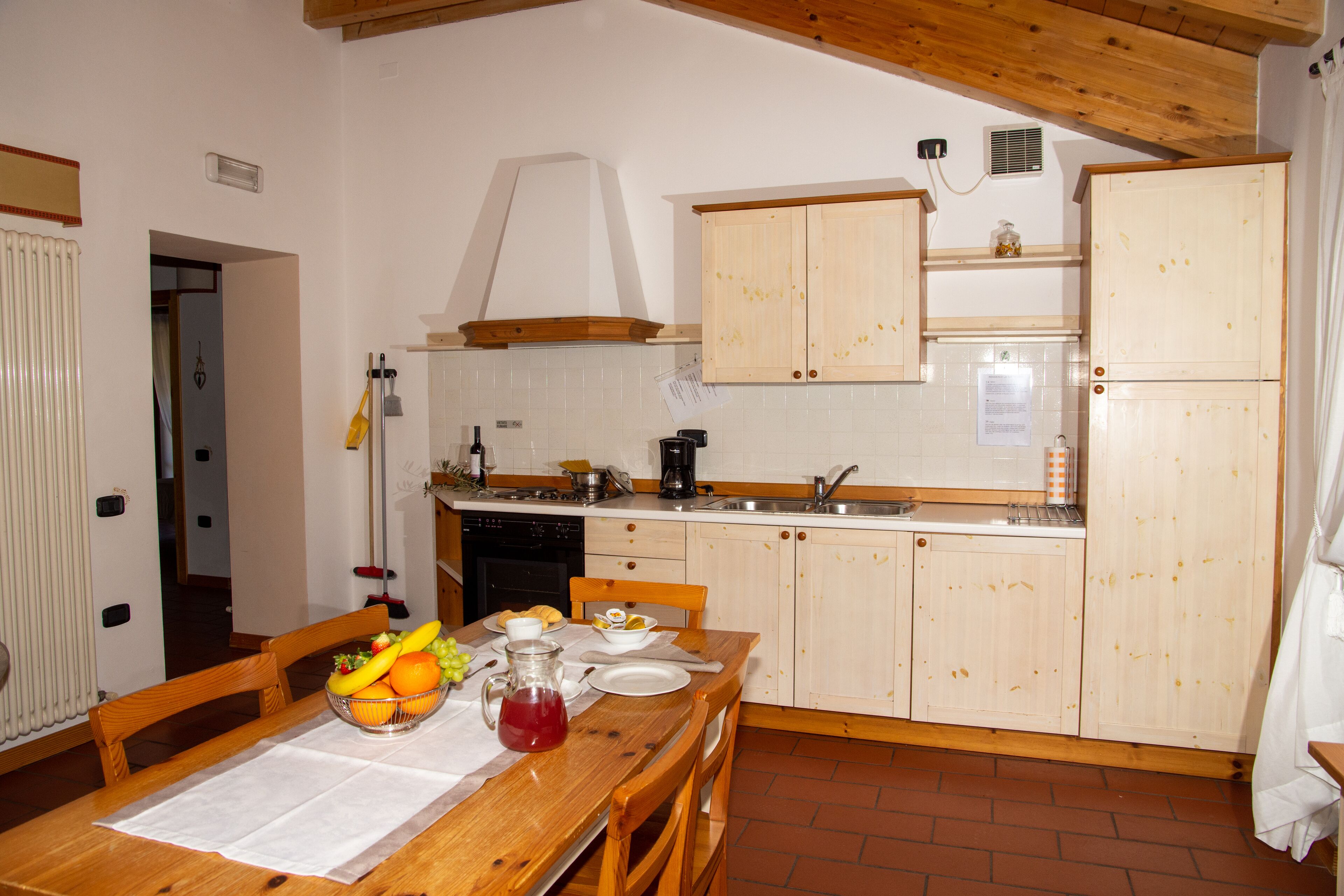 A kitchen with wooden cabinets, a dining table set with plates, a fruit bowl, and a pitcher.