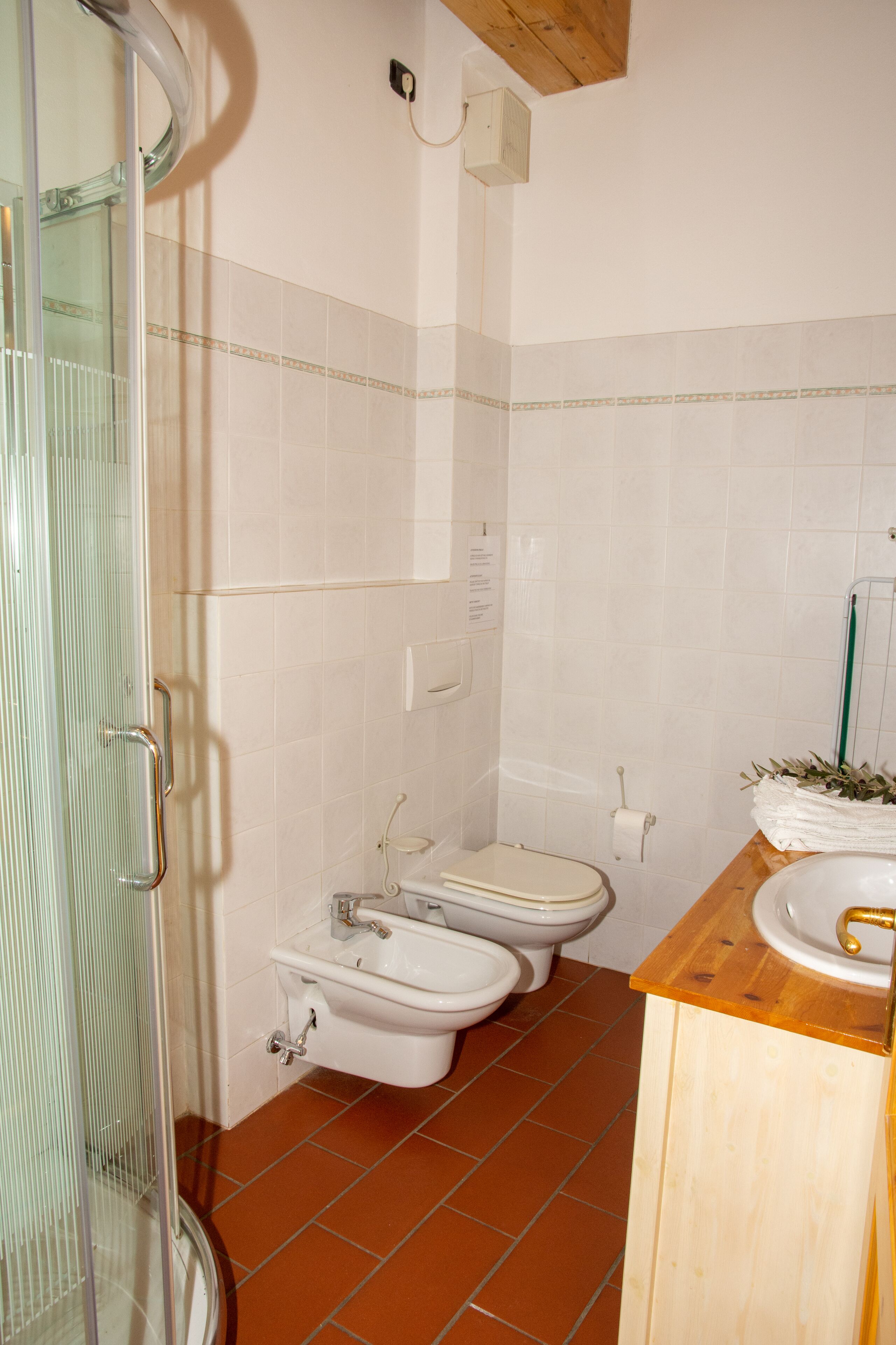 A bathroom with a glass shower enclosure, two toilets, a sink, and a wooden countertop.