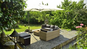 A patio with wicker furniture, a stone pathway, and a large umbrella. - Pazo Torre do Barrio (Sarria)