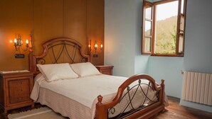 A bedroom with a wooden bed, nightstands, wall sconces, and a window with a view. - Pazo Torre do Barrio (Sarria)