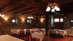 A rustic dining area with stone walls, wooden beams, and multiple tables with white tablecloths. - Pazo Torre do Barrio (Sarria)