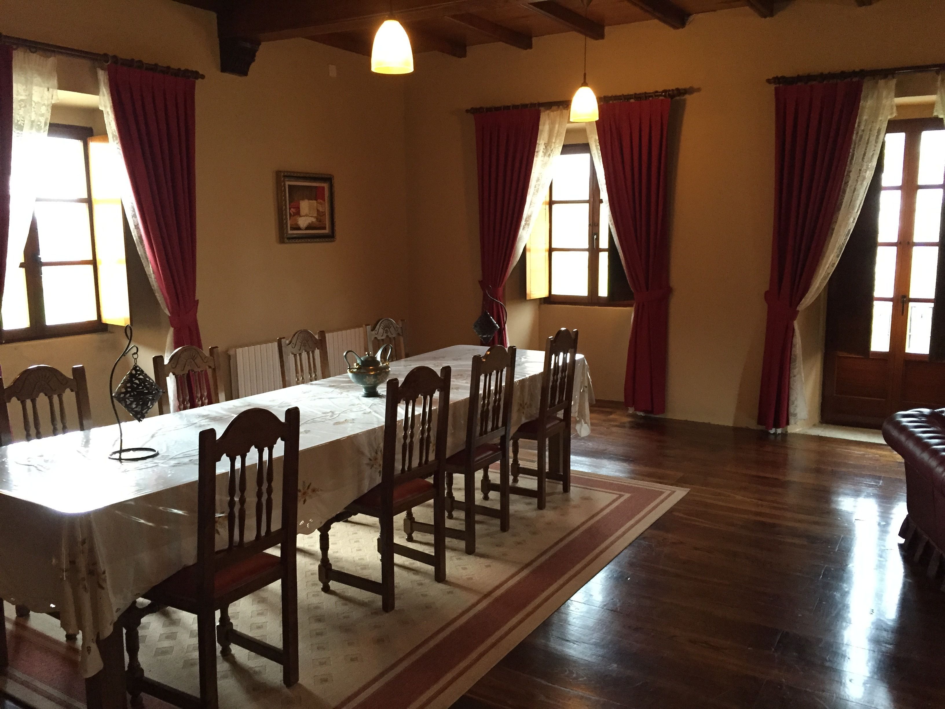 Une salle à manger avec une longue table, des chaises en bois et des rideaux rouges.