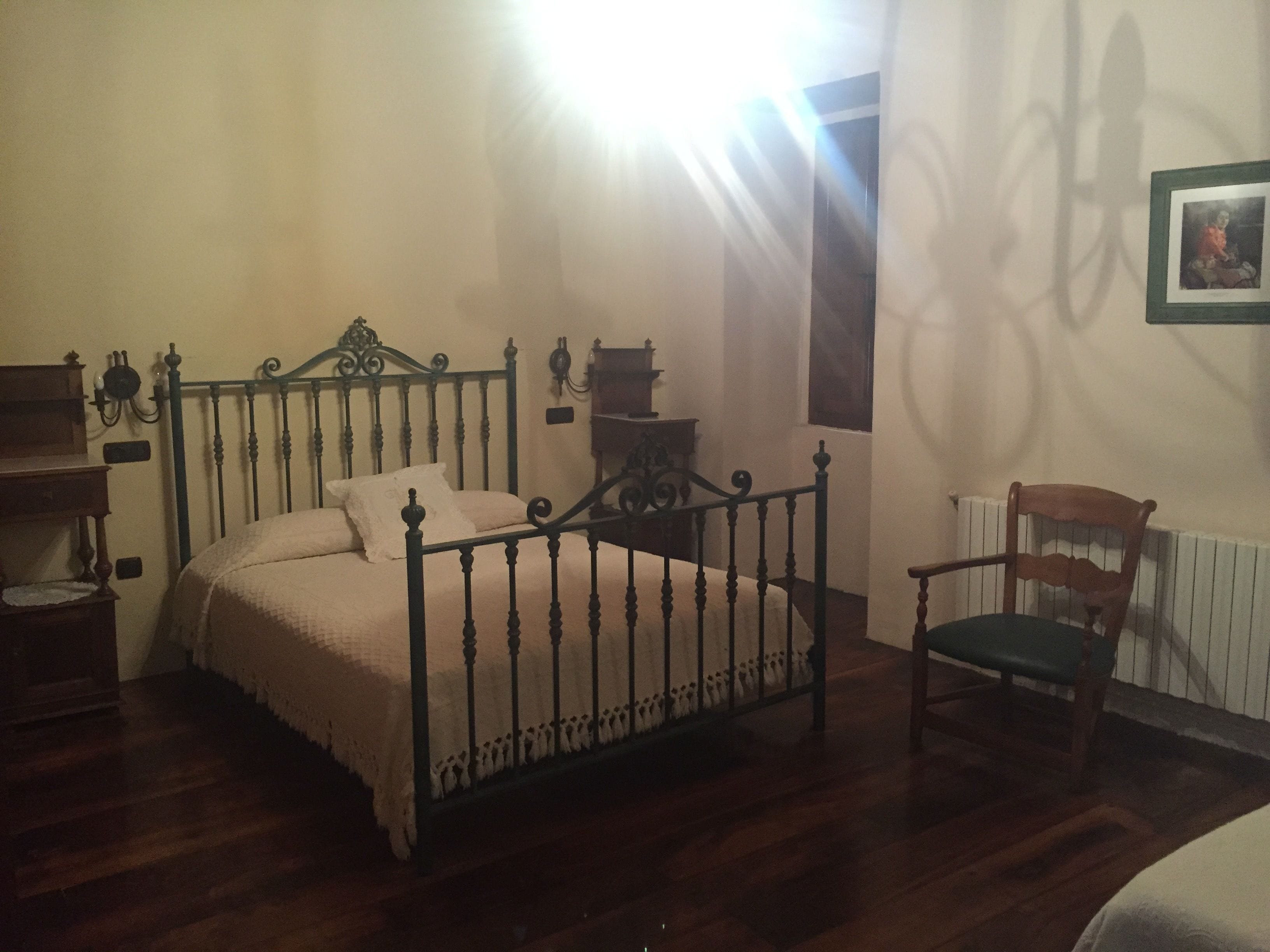 A bedroom with a bed, a chair, a small table, and a radiator.