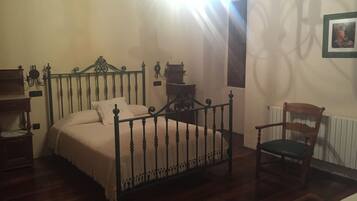 A bedroom with a bed, a chair, a small table, and a radiator.