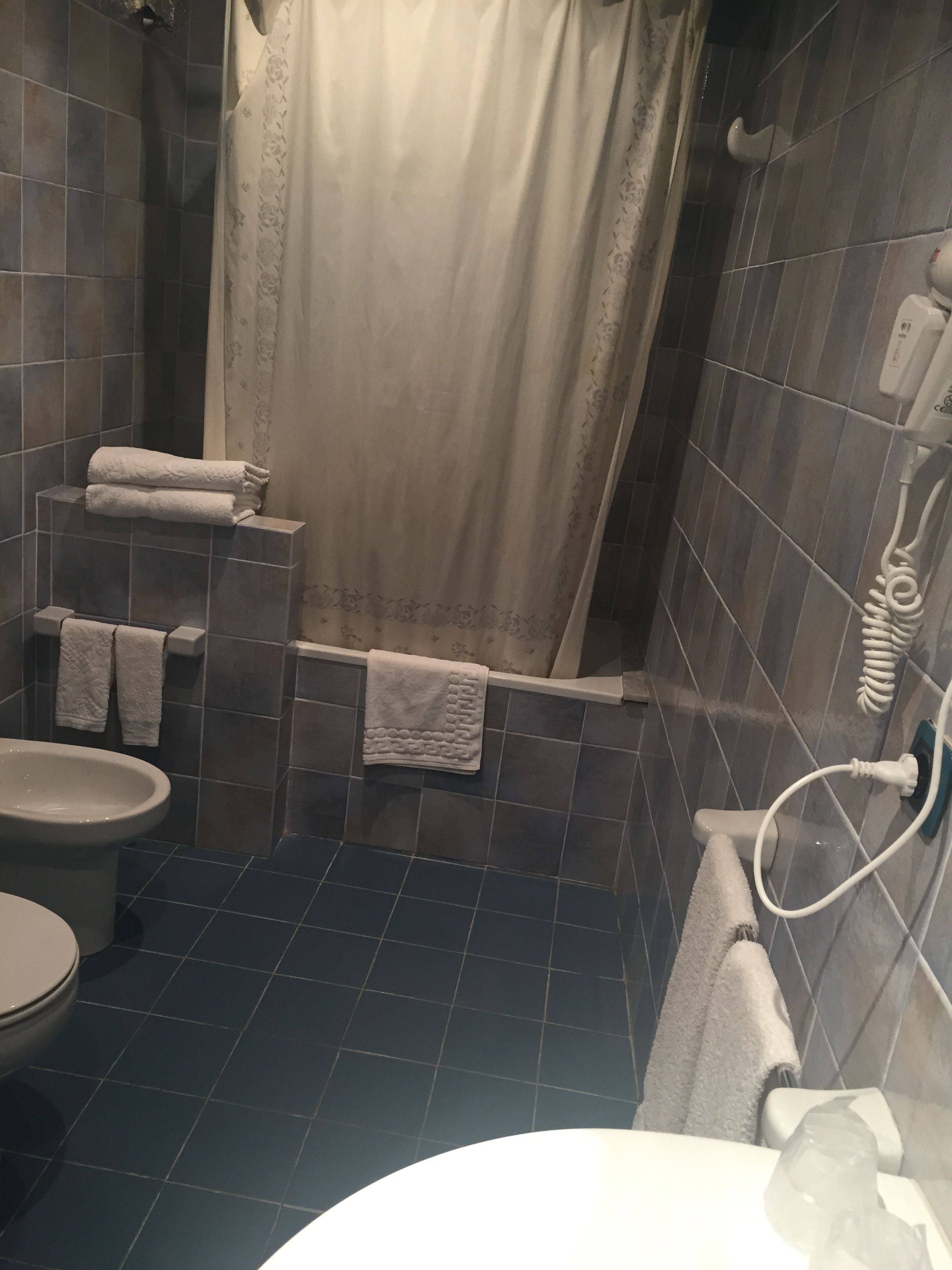 A bathroom with a shower, toilet, and sink. There are towels hanging on the wall and a shower curtain.