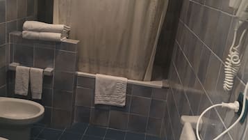 A bathroom with a shower, toilet, and sink. There are towels hanging on the wall and a shower curtain.