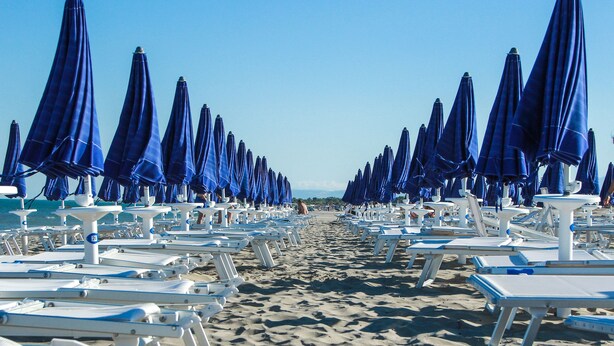Una playa con filas de tumbonas blancas y sombrillas azules.