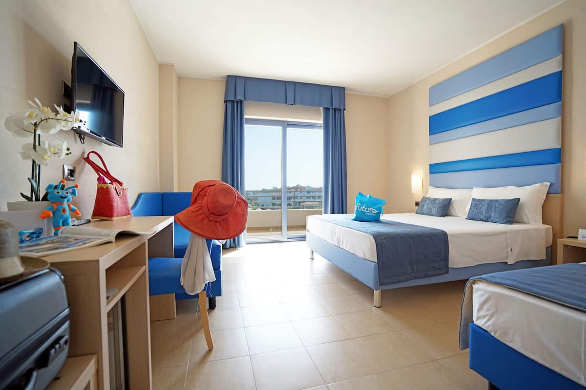 A hotel room with a bed, a desk, a chair, a television, and a view of the outside.