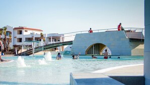 Una piscina con agua azul cristalina, un tobogán y una zona cubierta con gente.