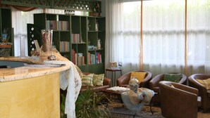 Una sala de estar acogedora con una mesa de centro de madera, sillones de cuero, una estantería y un ventanal con cortinas ligeras.
