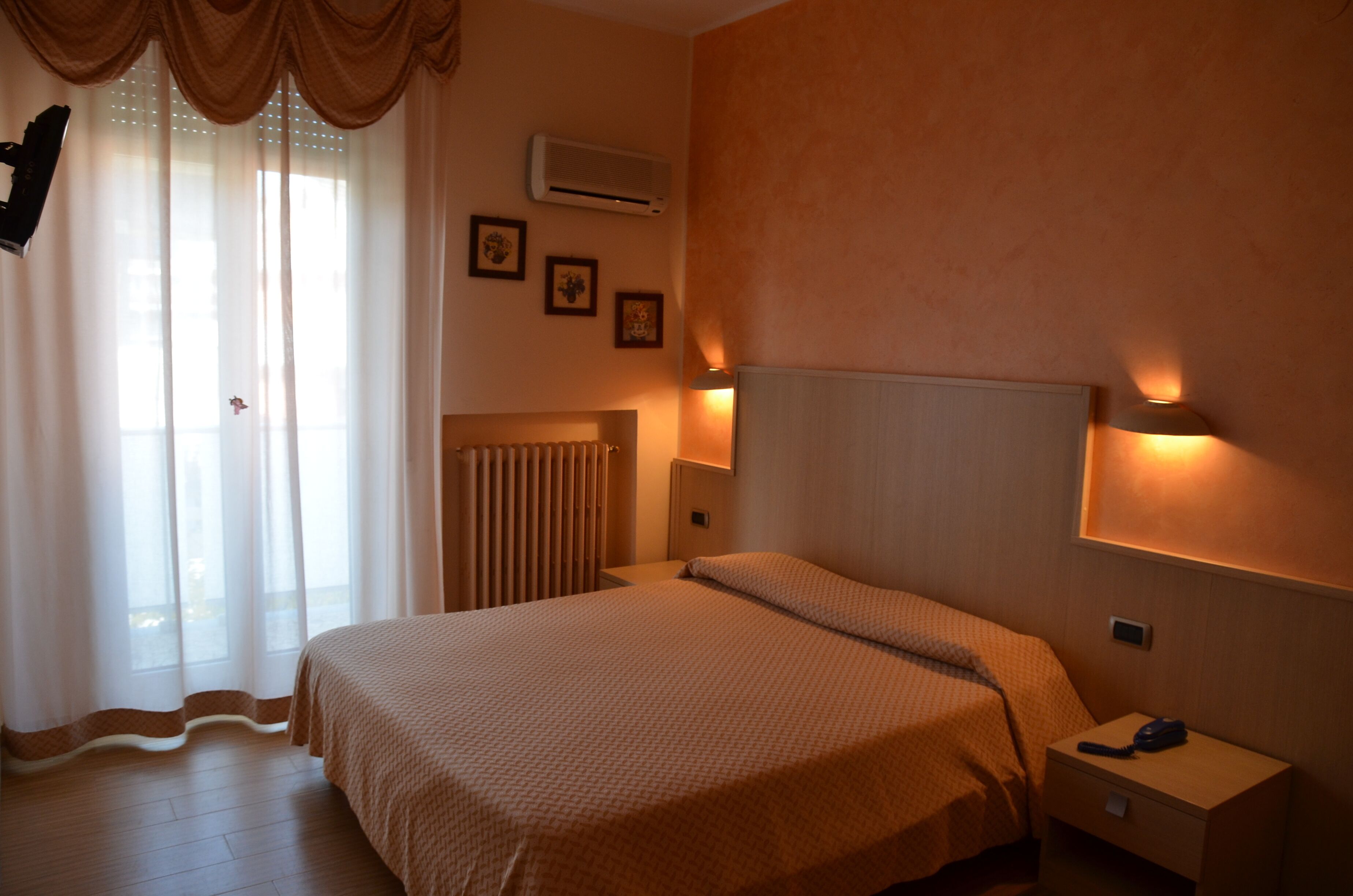 Una camera d'albergo con un letto, una lampada da comodino, un comodino, un condizionatore d'aria e tende.