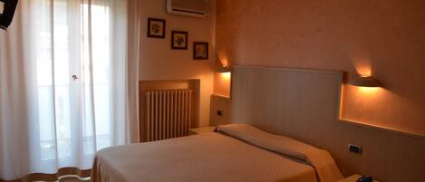 Una camera d'albergo con un letto, una lampada da comodino, un comodino, un condizionatore d'aria e tende.