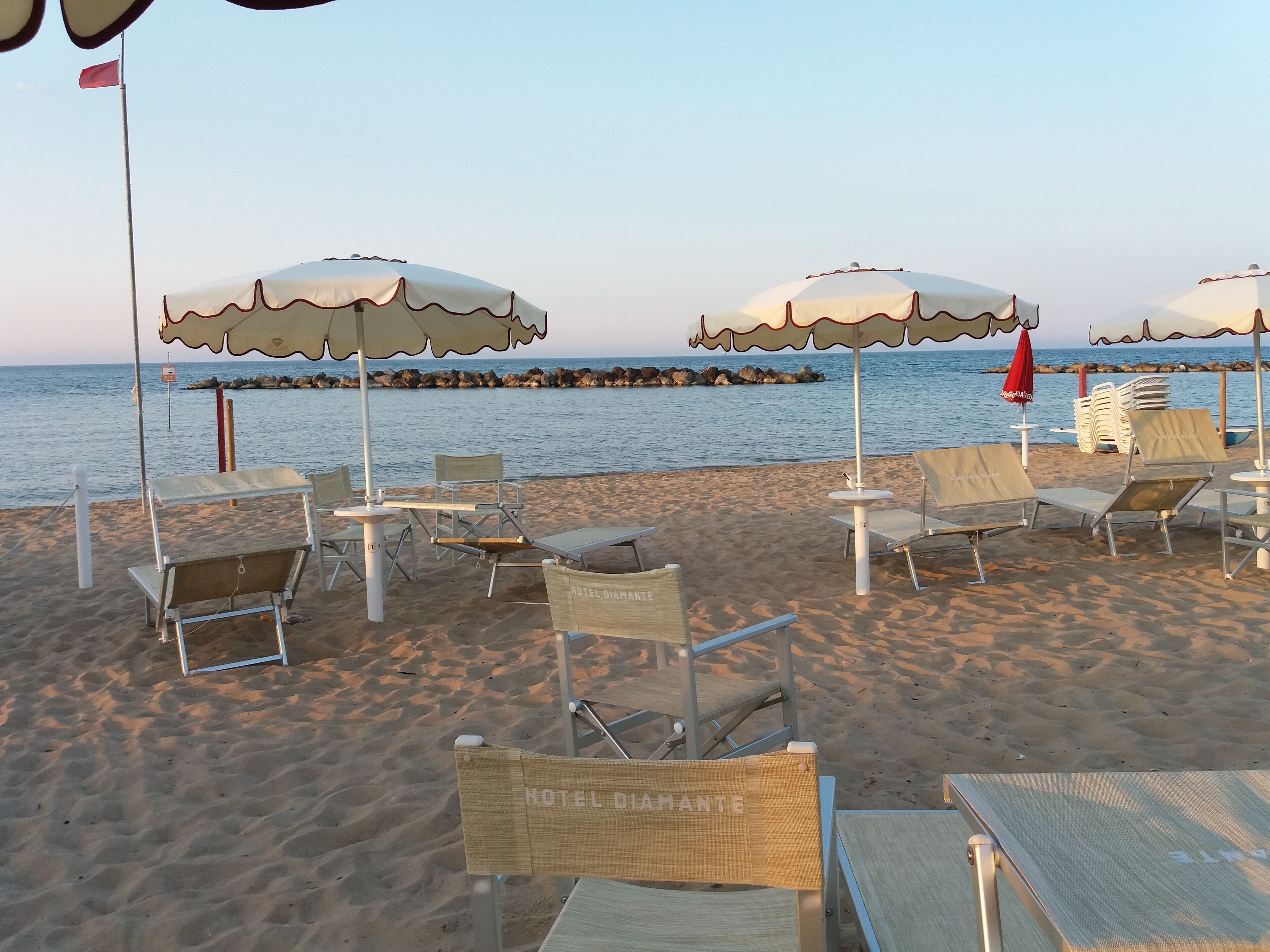 Un'area relax in spiaggia con ombrelloni e lettini, una bandiera e vista sul mare.