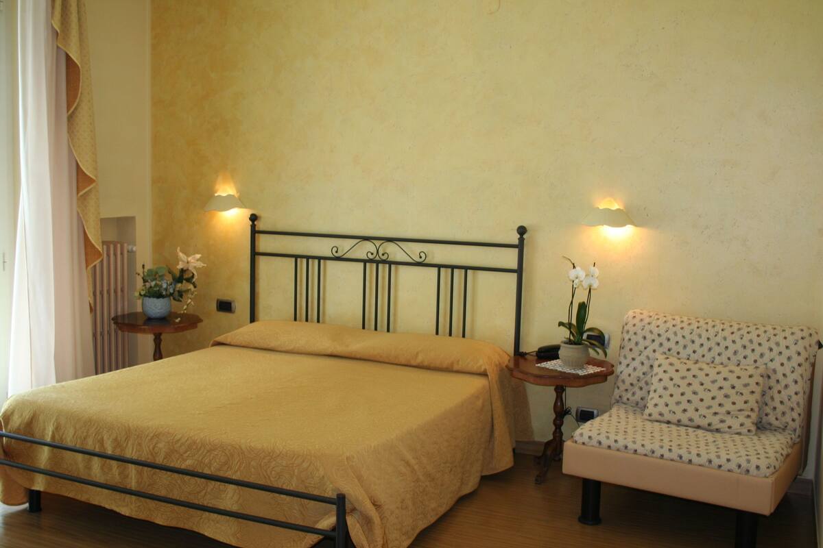 Un dormitorio ordenado con cama, una silla y dos mesitas de noche con lámparas.