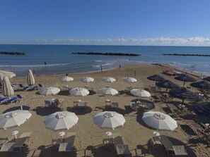 Een strand met rijen ligbedden en parasols, een heldere lucht en een rustige zee.