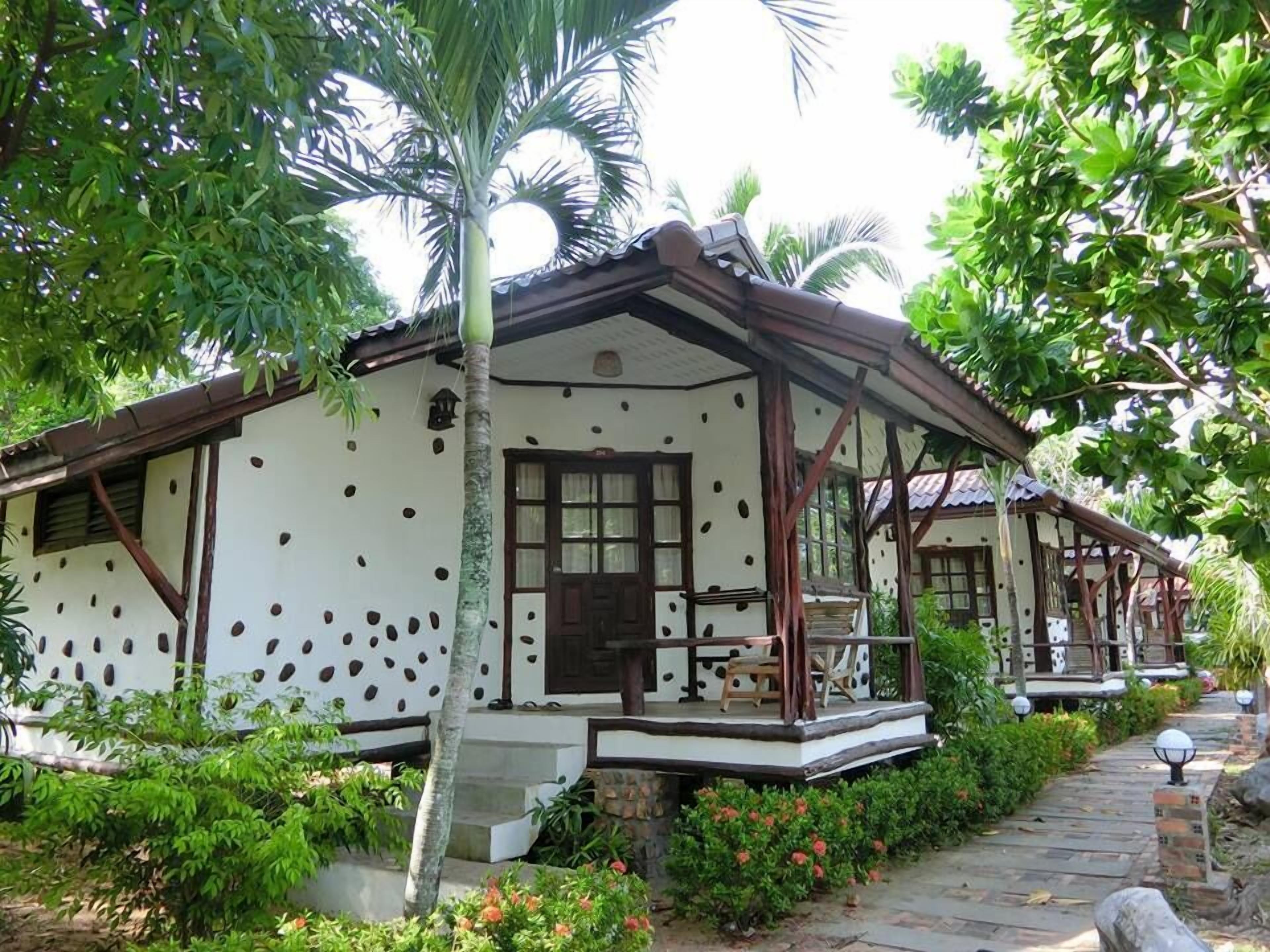 A traditional house with a porch, surrounded by lush greenery and a stone pathway.