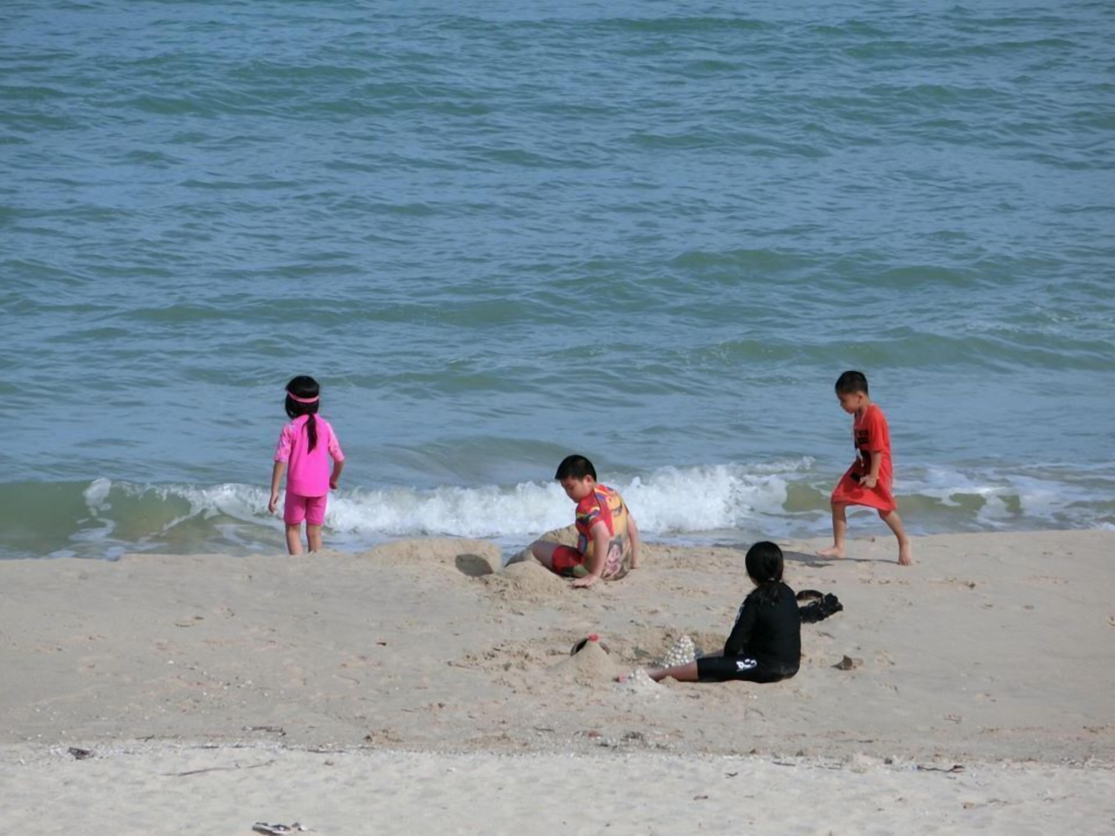 Three children playing on a sandy beach with waves in the background.