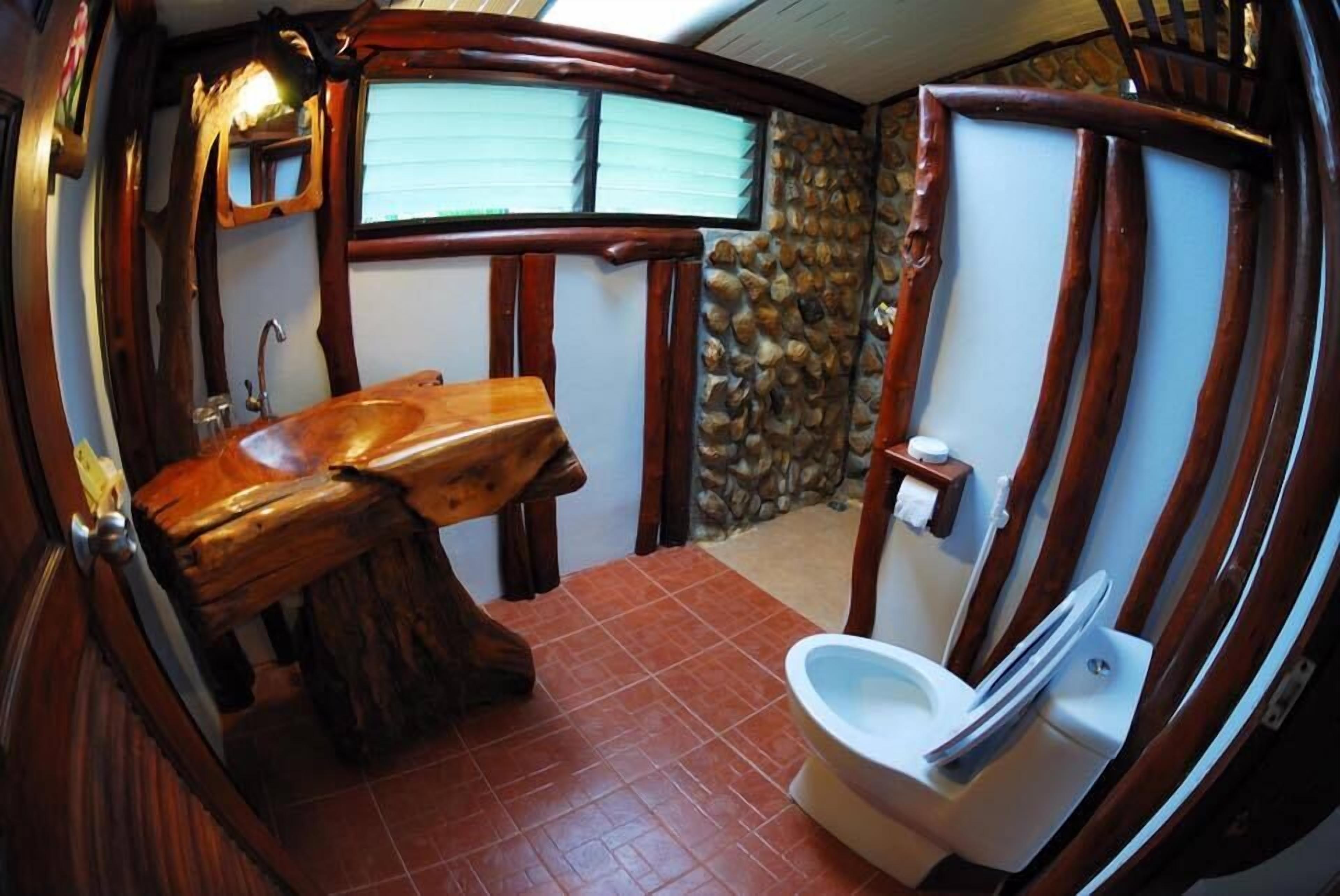 A rustic bathroom with a wooden sink, a stone wall, and a white toilet.