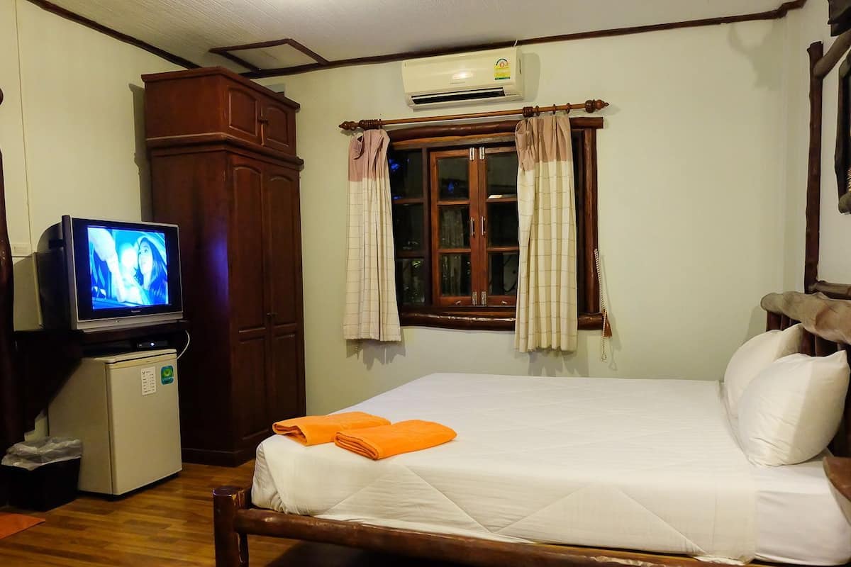 A room with a bed, a television, a small refrigerator, and a window with curtains.