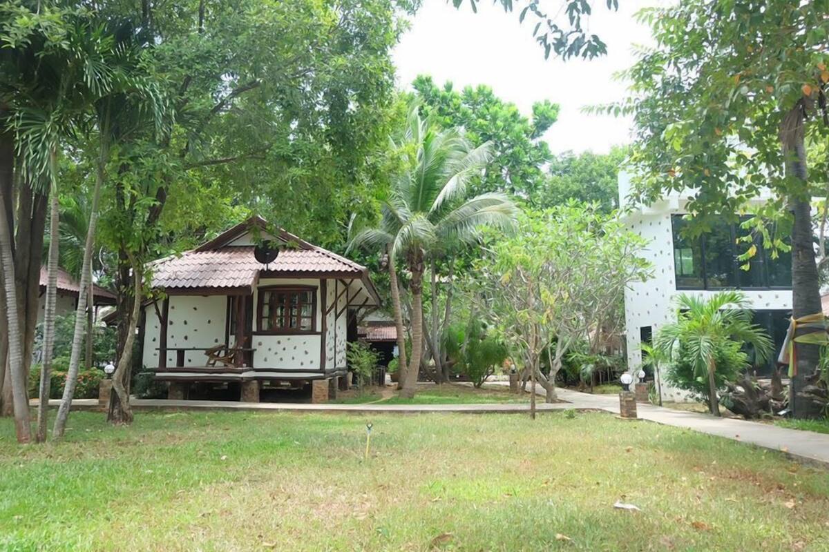 A traditional wooden house with a tiled roof, surrounded by lush greenery and palm trees.