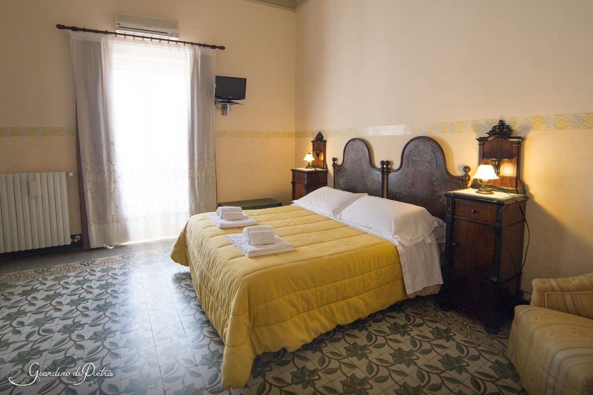 Een hotelkamer met een bed, twee nachtkastjes met lampen, een radiator, een televisie aan de muur en een kamer met een patroon vloer.