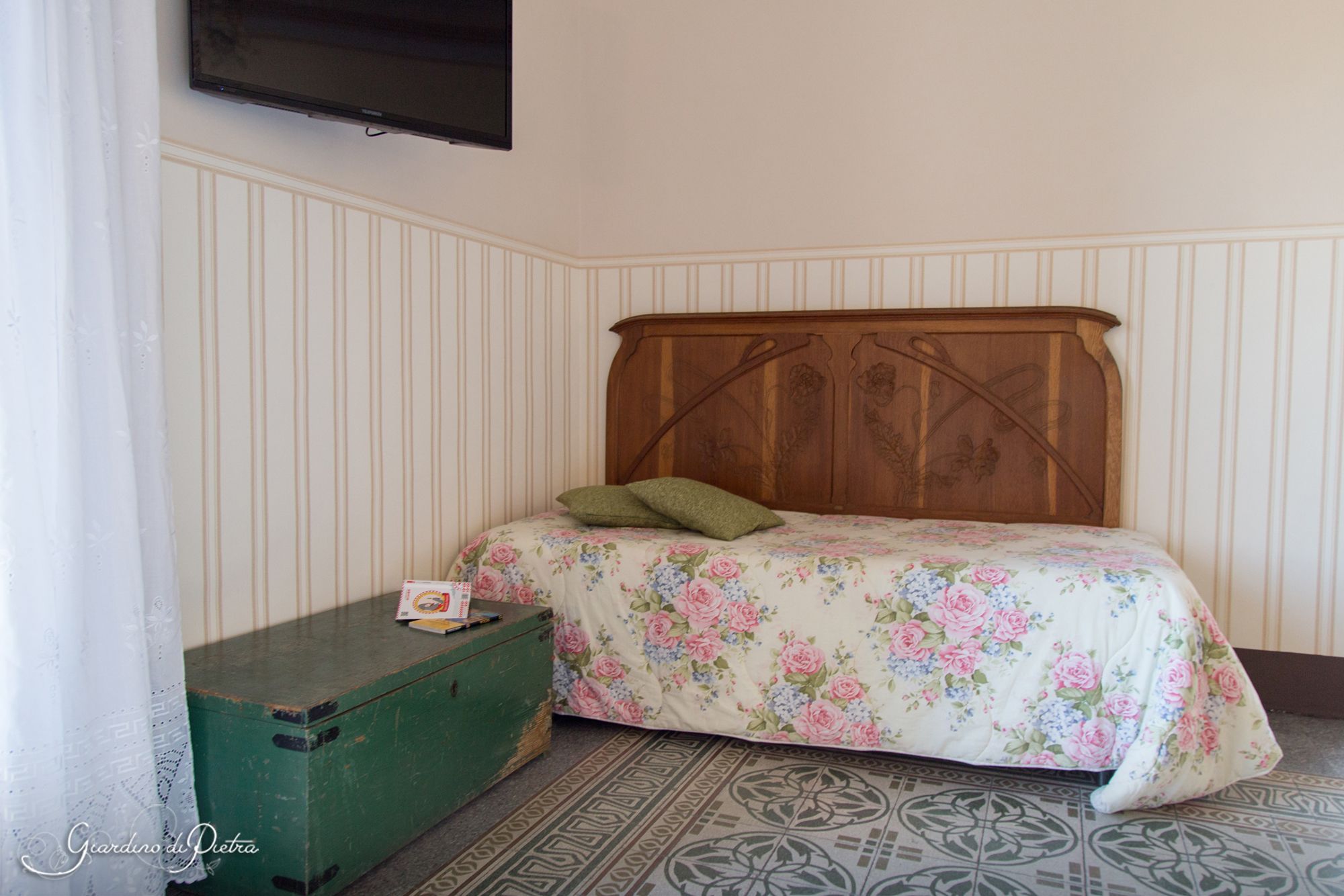 A bedroom with a wooden headboard, a floral bedspread, a green chest of drawers, and a patterned rug.
