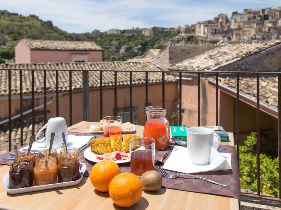 Una mesa de desayuno con diversos alimentos y bebidas en un balcón con vistas a un paisaje urbano.
