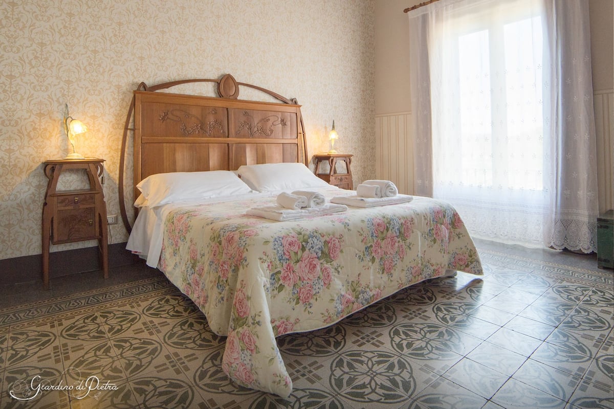 Een opgemaakt bed met bloemenbedrukking, twee nachtkastjes en een vloer met patroon.