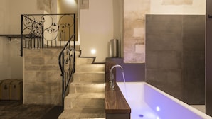 A bathroom with a bathtub, a wooden bench, and a stone staircase. - Giardino di Pietra (Ragusa)