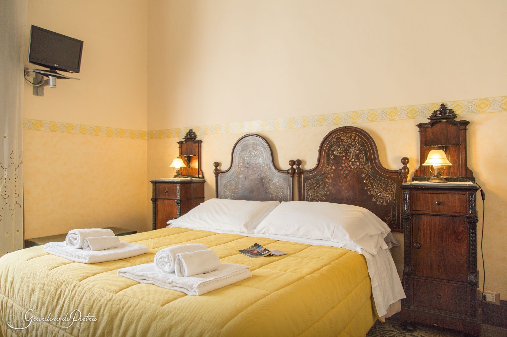 A hotel room with a bed, two bedside tables with lamps, a television on the wall, and a patterned border on the wall.