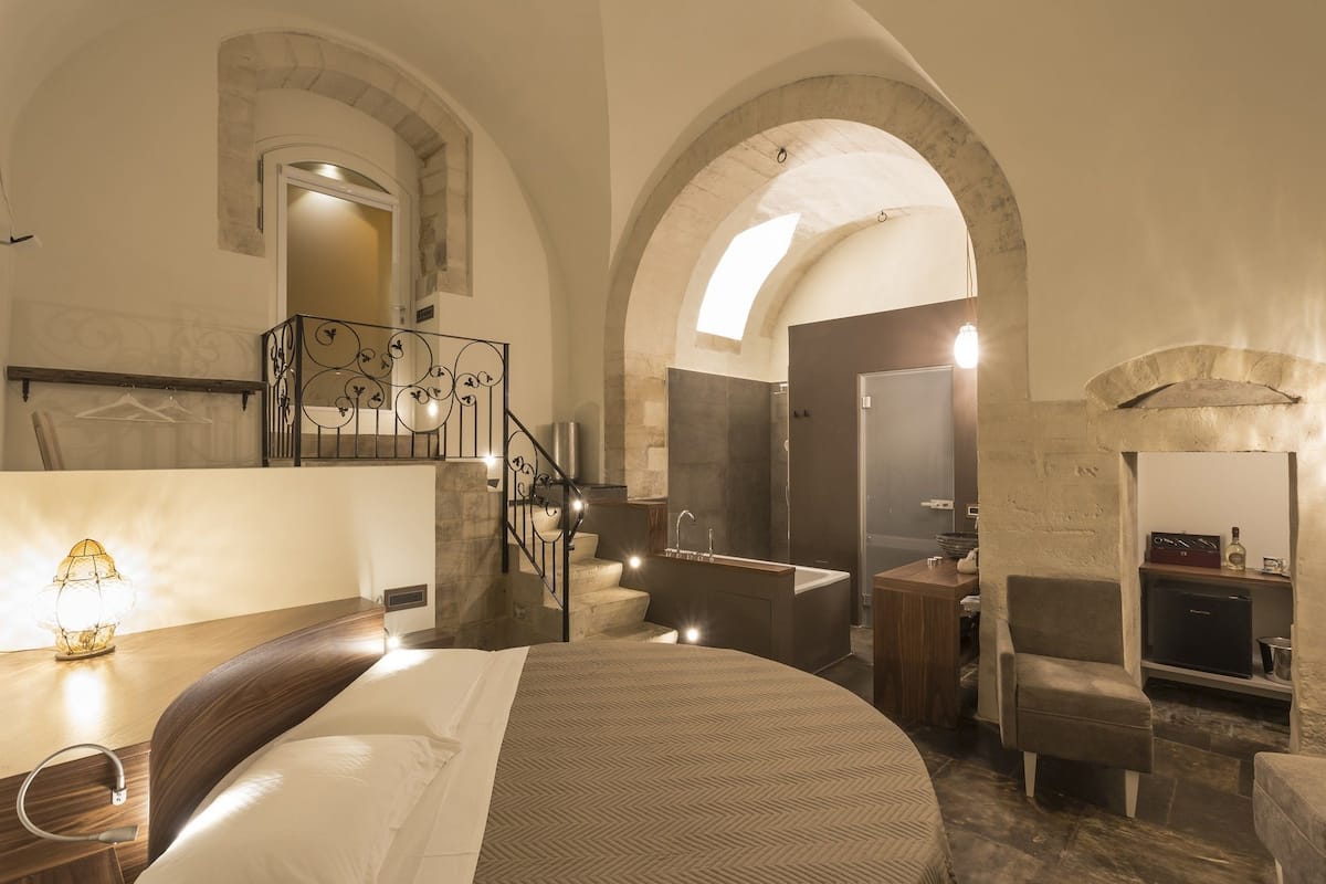 Een ruime slaapkamer met een groot bed, een zithoek, een badkamer en een stenen openhaard.