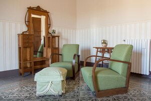 Una habitación con un armario de madera, dos sillones tapizados en verde, una mesita con un florero y un radiador.