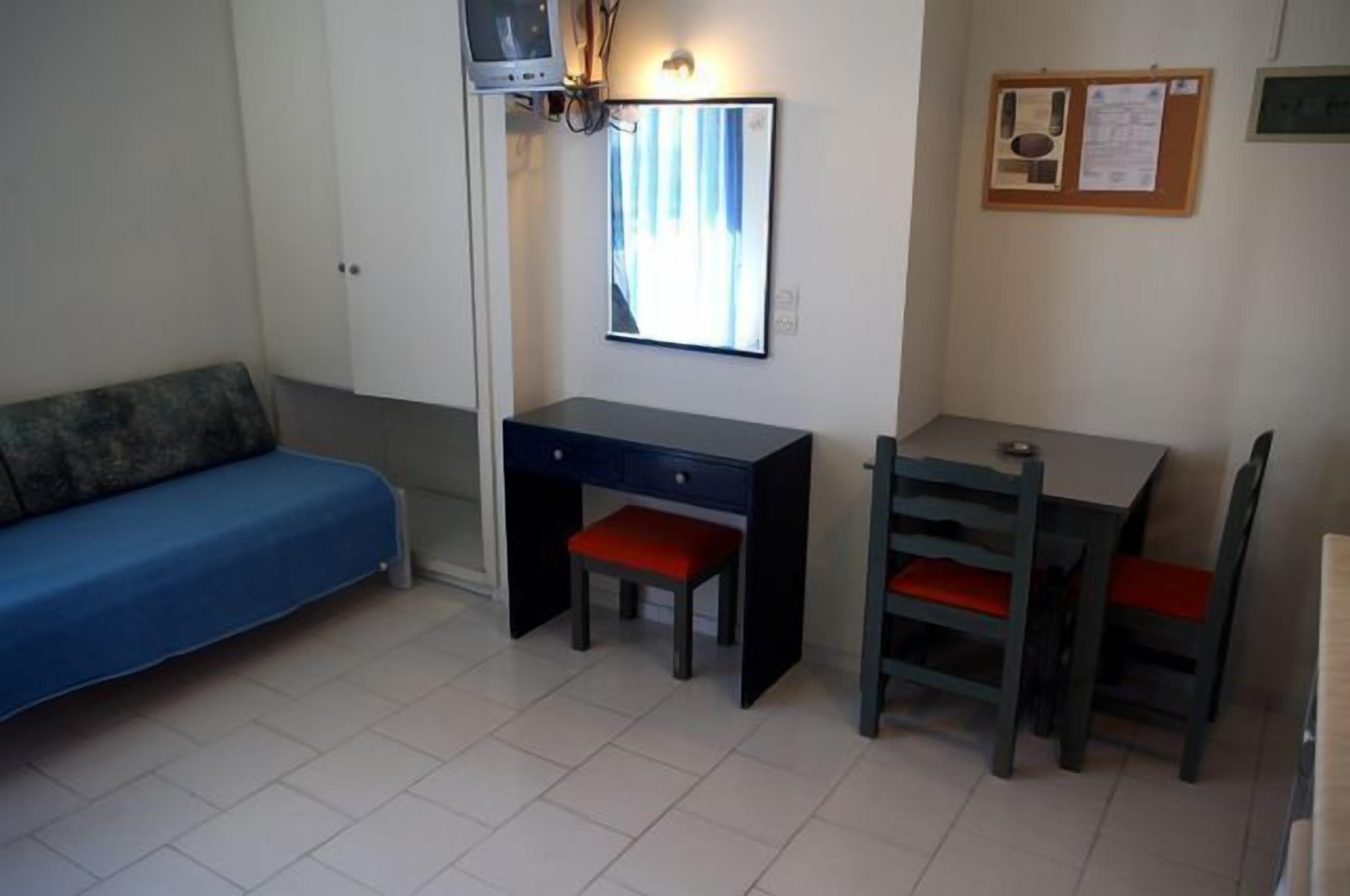 A small room with a blue sofa, a desk with two chairs, and a mirror on the wall.