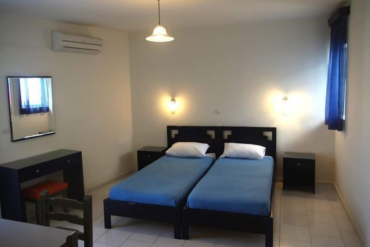 A room with two single beds, a desk, a chair, and a mirror.