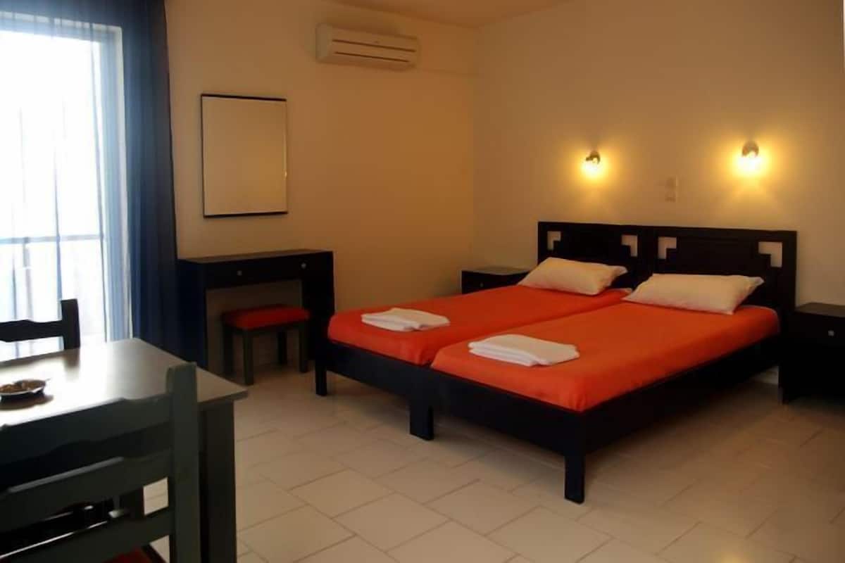 A hotel room with two beds, a desk, a chair, and a window with curtains.