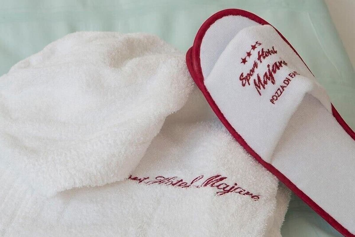 Un par de pantuflas con borde rojo y interior blanco. Las pantuflas tienen texto bordado en el lateral.
