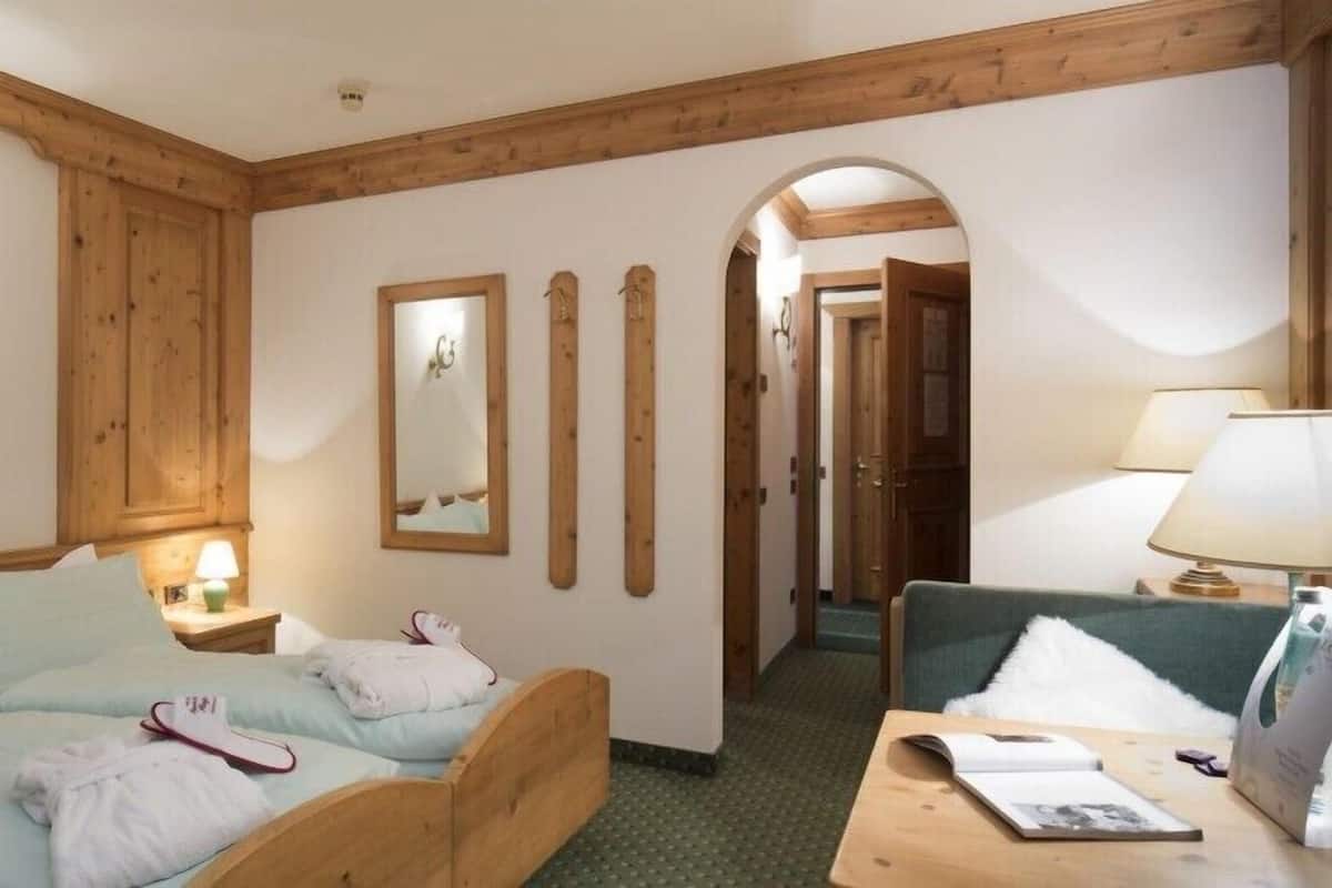 Habitación de hotel con una cama de madera, un escritorio con lámpara, un espejo y un sofá verde.