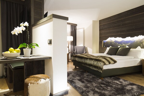 A modern bedroom with a bed, a desk, a chair, and a large window with a mountain view.