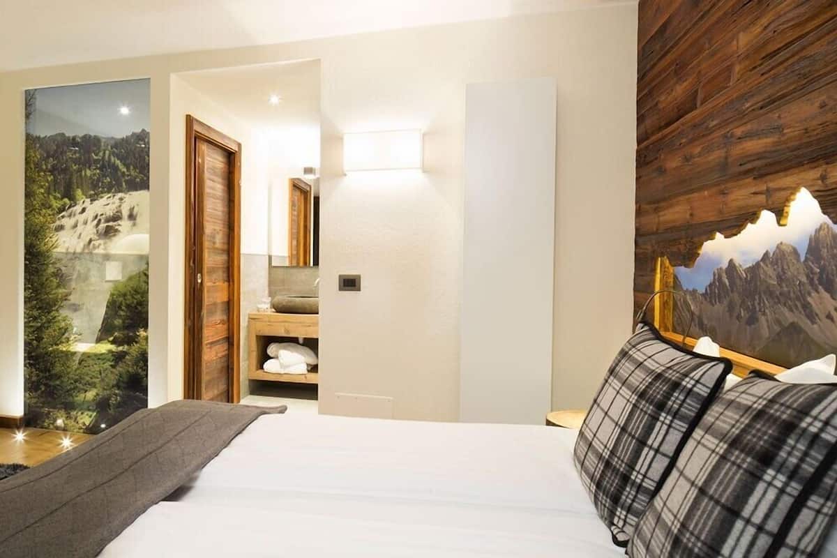 Un dormitorio con cama, cabecera de madera, mesita de noche, lámpara de pared y puerta que da al baño.