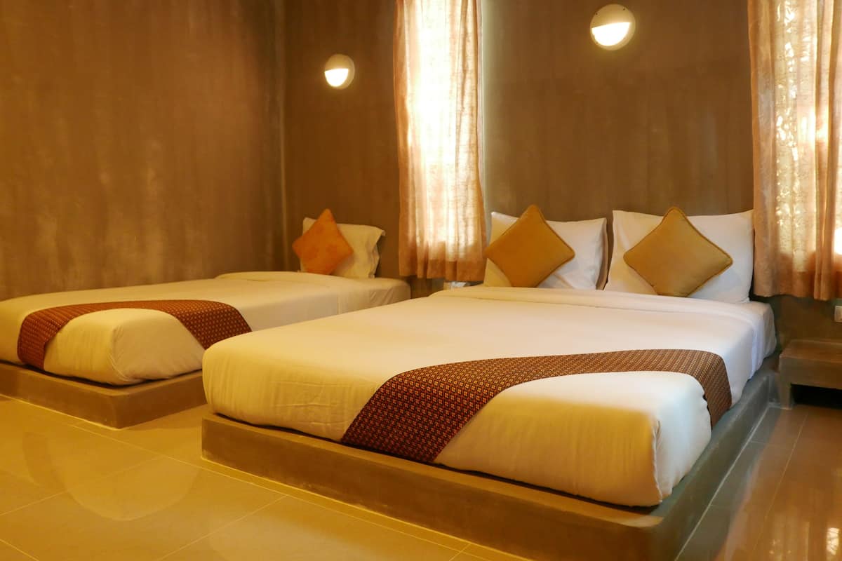 A hotel room with two beds, each with white linens and brown decorative pillows. There are two wall-mounted lights and a window with curtains.