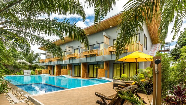 A modern hotel with a large swimming pool, wooden balconies, and lush tropical landscaping. - Le Pes Villas (Khanom)