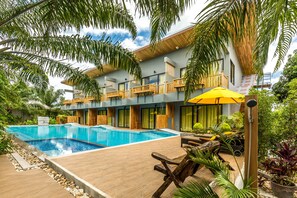 Un hotel moderno con una amplia piscina, balcones de madera y exuberante jardinería tropical.